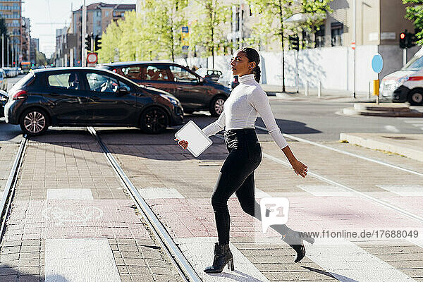 Young businesswoman crossing road by cars on sunny day