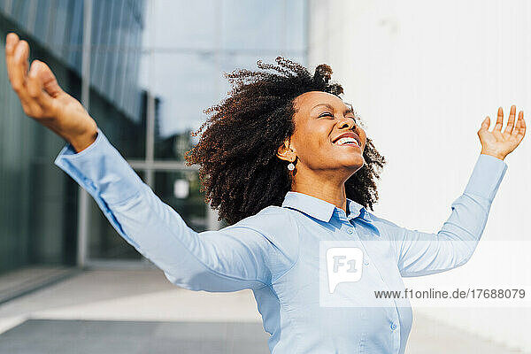 Happy businesswoman with arms outstretched enjoying dance on sunny day