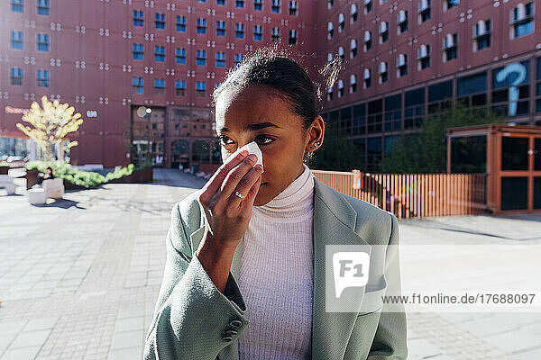 Sad businesswoman wiping tears with tissue in front of office building