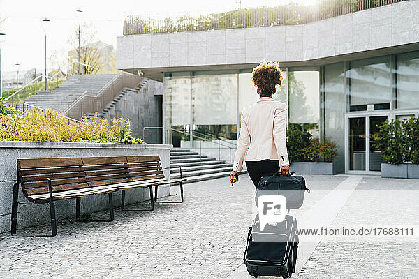 Businesswoman walking with luggage on footpath