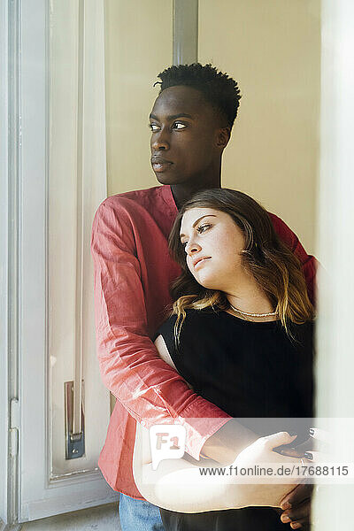 Young couple standing together by window at home