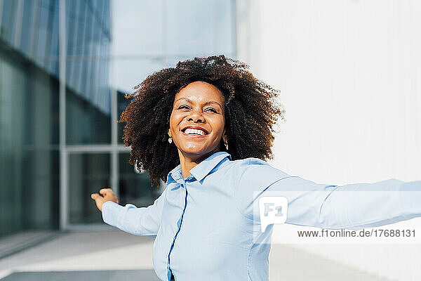 Happy businesswoman dancing with arms outstretched on sunny day