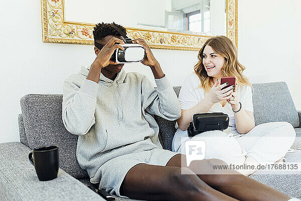 Man wearing virtual reality simulator sitting by girlfriend on sofa at home