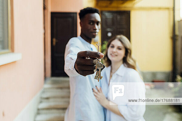Young man with girlfriend showing keys standing in front of house
