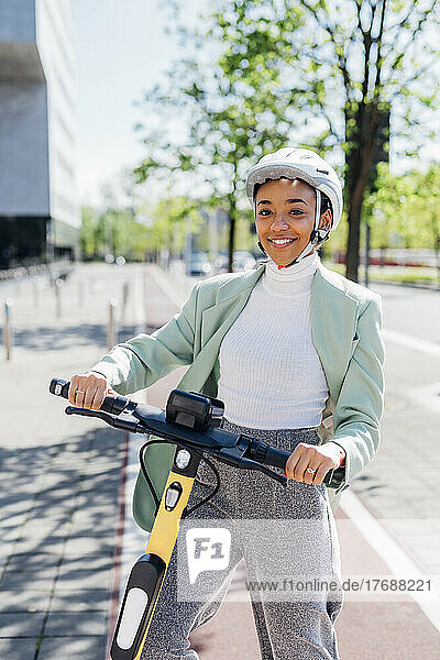 Smiling businesswoman with electric push scooter on footpath