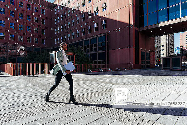 Young businesswoman with laptop walking in downtown district