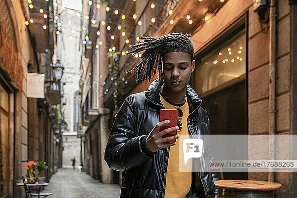 Young man wearing leather jacket using smart phone standing in alley