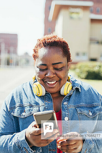 Happy woman with wireless headphones using smart phone in the street