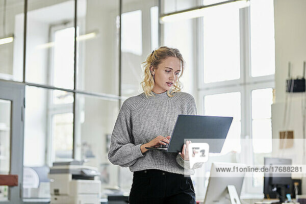 Junge Frau steht mit Laptop im Büro