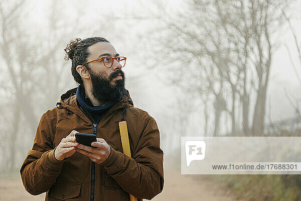Mature man wearing eyeglasses holding smart phone lost in forest