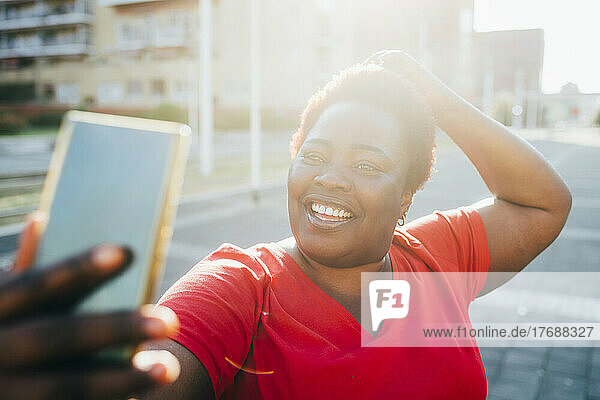 Happy woman taking selfie through smart phone on sunny day