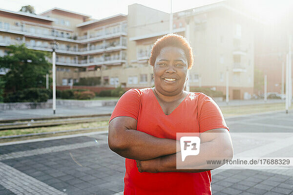 Smiling woman standing with arms crossed on sunny day