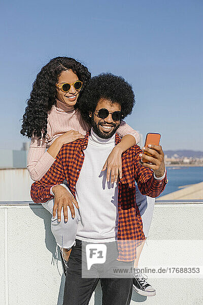 Happy couple taking selfie through mobile phone on sunny day