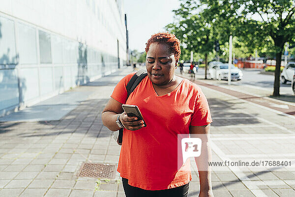 Woman using smart phone walking on footpath