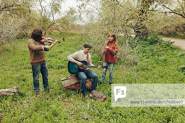 Man practicing guitar with friends playing violin and clarinet in field