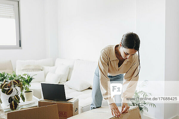 Young woman unpacking cardboard box in living room at home