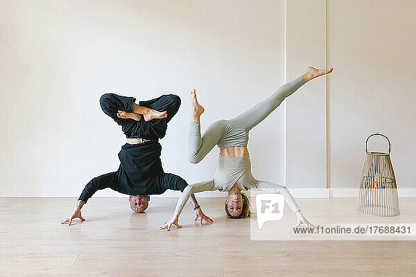 Friends practicing headstand poses in front of wall at yoga studio