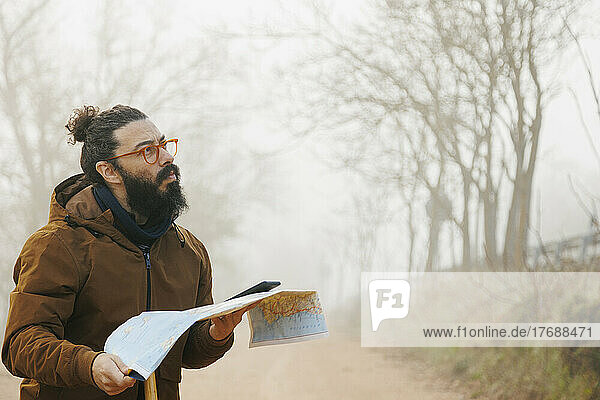 Mature bearded man wearing eyeglasses standing with map in forest