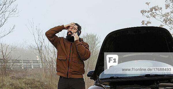 Worried man talking on mobile phone standing by car