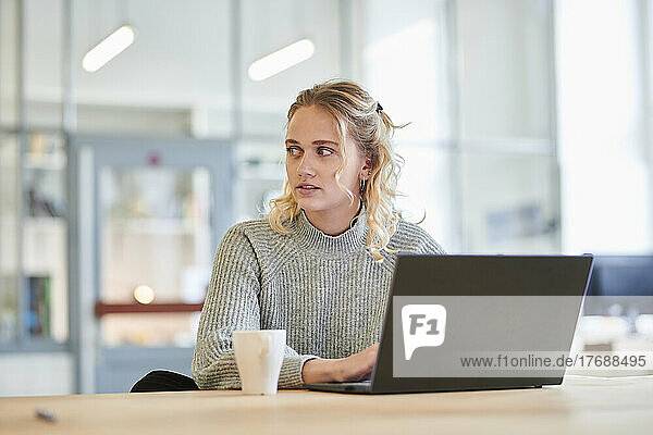 Junge Frau sitzt mit Laptop am Schreibtisch im Büro