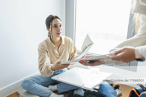 Young woman with instruction manual installing new furniture at home