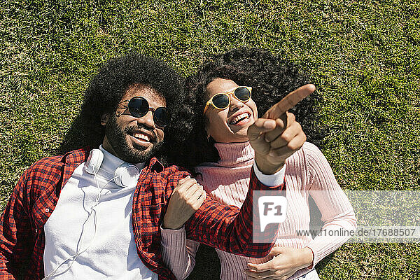 Smiling boyfriend pointing lying on grass next to girlfriend