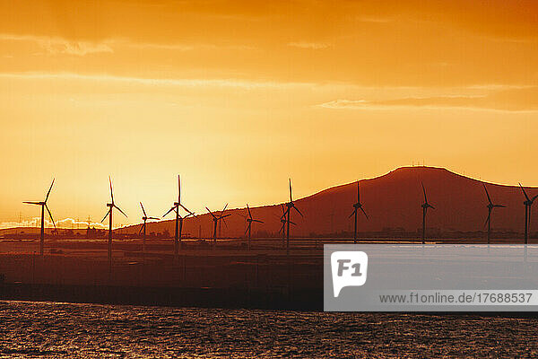 Silhouette wind turbines in front of mountain at sunset