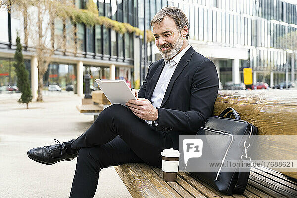 Smiling mature businessman using tablet PC sitting on bench