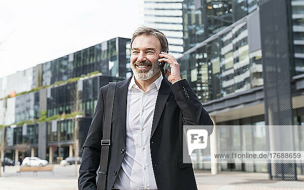 Glücklicher Geschäftsmann  der vor dem Bürogebäude mit dem Mobiltelefon spricht