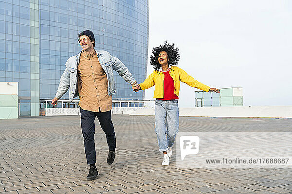 Cheerful couple holding hands running together on footpath