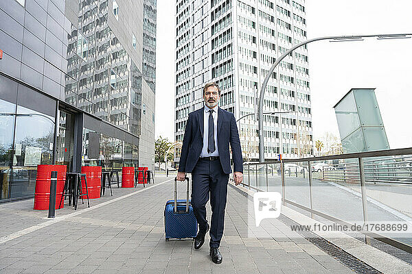Businessman with suitcase walking on footpath