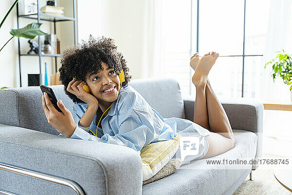 Beautiful woman with headphones and smart phone lying on sofa at home