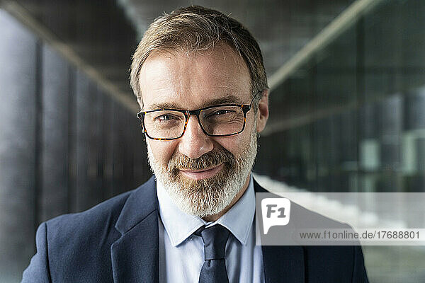 Smiling mature businessman wearing eyeglasses standing in corridor