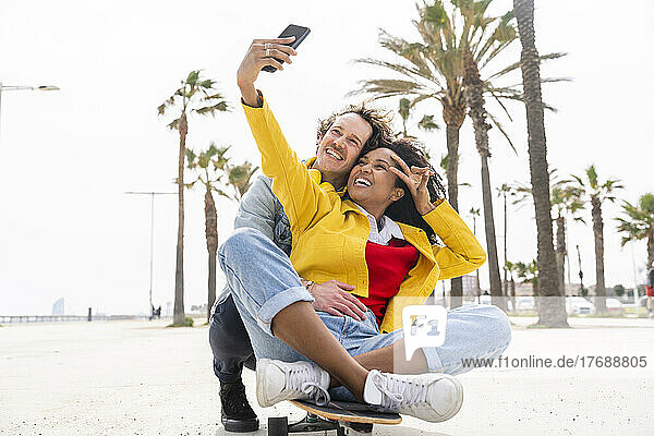 Glückliche Frau mit Mann macht Selfie per Smartphone auf Skateboard