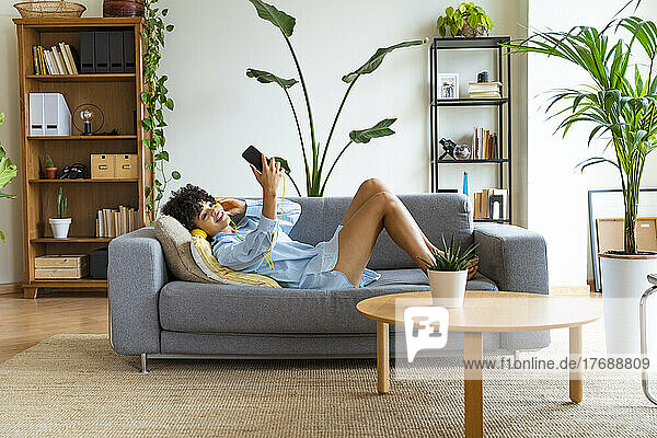 Smiling woman taking selfie through smart phone lying on sofa at home