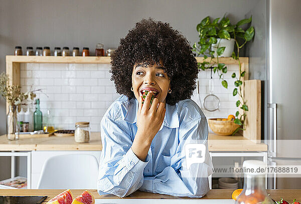 Schöne Frau isst Erdbeeren und lehnt sich zu Hause an die Kücheninsel