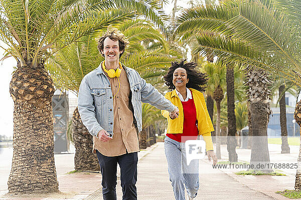 Happy man with woman walking in front of trees on footpath