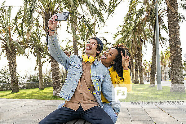 Glückliches Paar streckt die Zunge heraus und macht im Park ein Selfie mit dem Handy