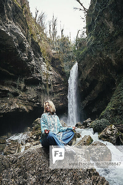 Mature woman sitting on rock in front of waterfall
