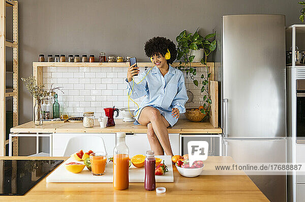 Glückliche Frau  die zu Hause auf der Küchentheke sitzt und ein Selfie mit ihrem Smartphone macht