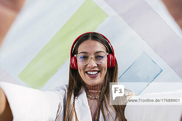 Happy woman wearing wireless headphones in front of wall