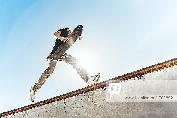Mann mit Skateboard läuft an sonnigem Tag im Skateboardpark