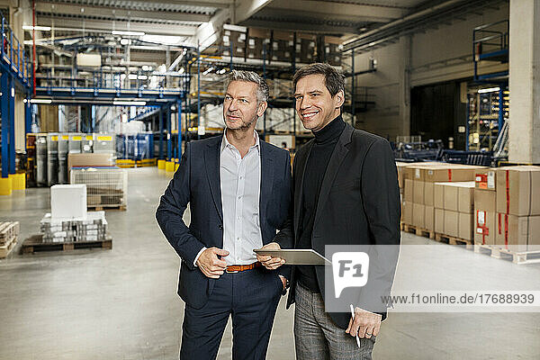 Confident businessman with colleague holding tablet PC in warehouse