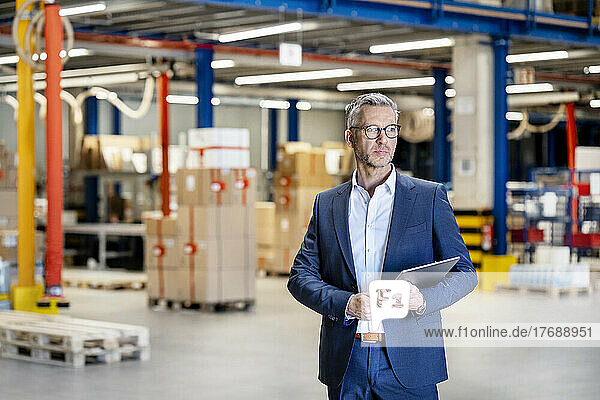 Confident businessman with tablet PC standing in factory