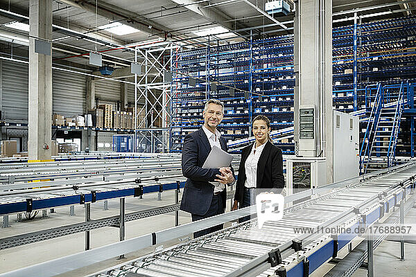 Confident business people by conveyor belt in warehouse