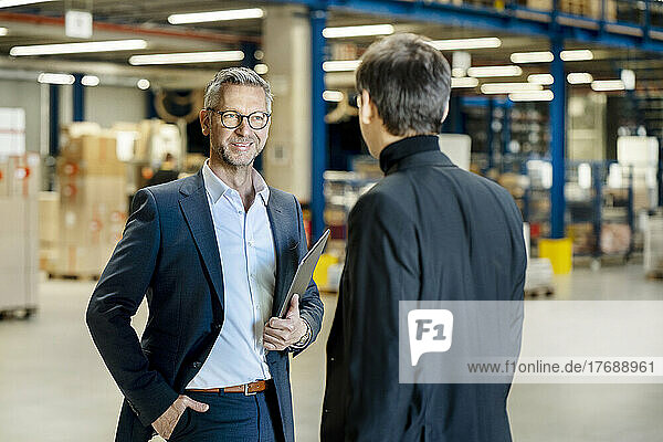 Mature businessman with hand in pocket discussing with colleague in factory
