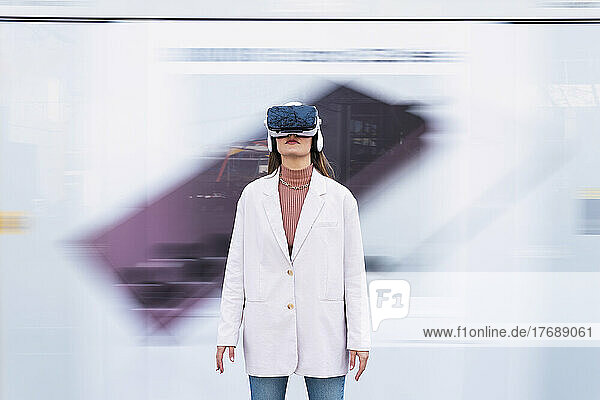 Businesswoman wearing virtual reality simulator standing in front of wall