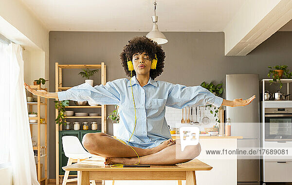 Woman with arms outstretched meditating on dining table at home