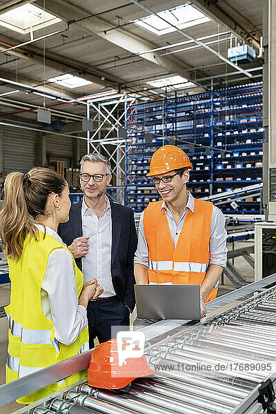 Young blue-collar worker discussing with businessman and colleague in warehouse