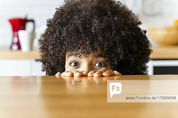 Woman with Afro hairstyle hiding behind kitchen island at home